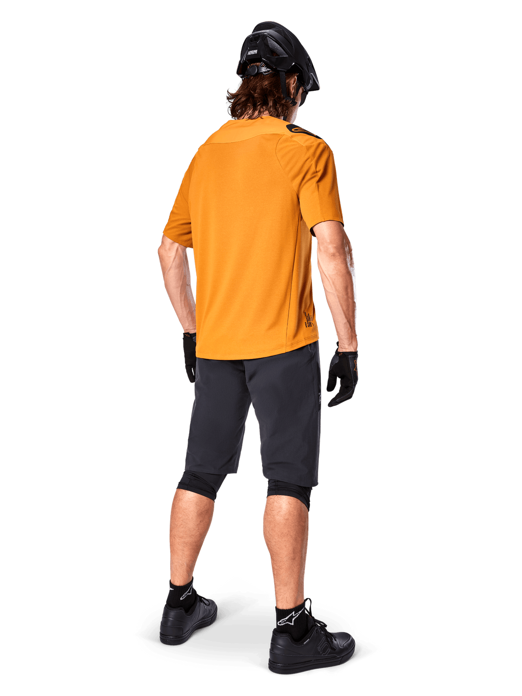 Alpinestars A-Aria Polartec Switch Jersey, jersey de MTB de manga corta, Dark Gold, vista trasera del modelo con pantalones cortos de montaña gris oscuro, casco negro y guantes, ropa técnica de ciclismo para senderos