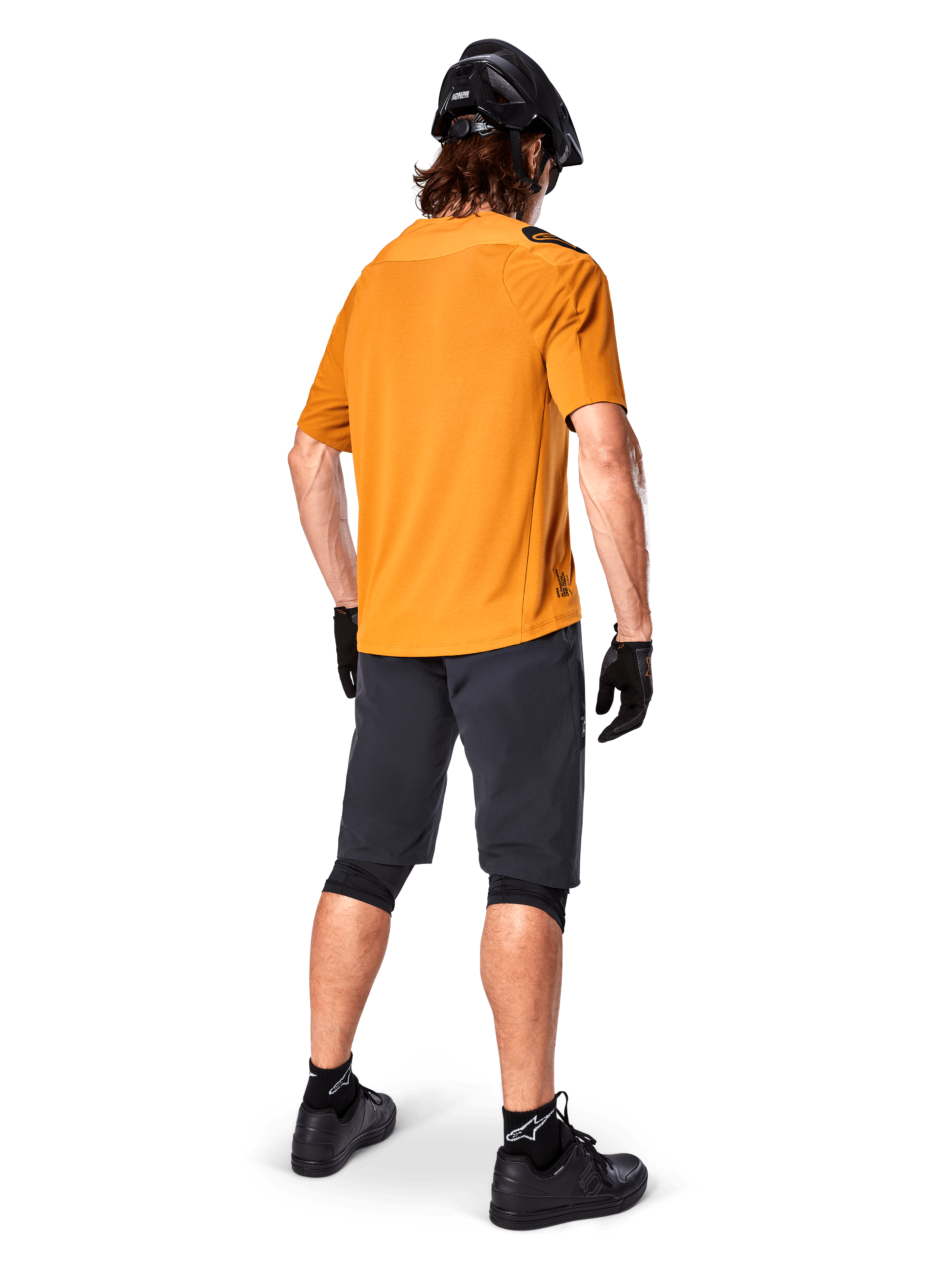 Alpinestars A-Aria Polartec Switch Jersey, jersey de MTB de manga corta, Dark Gold, vista trasera del modelo con pantalones cortos de montaña gris oscuro, casco negro y guantes, ropa técnica de ciclismo para senderos
