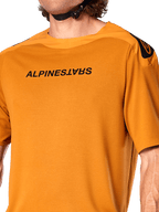 Jersey Alpinestars A-Aria Polartec Switch, camiseta de MTB de manga corta, color oro oscuro, con el logotipo de Alpinestars en negro invertido en el pecho, tejido técnico de alto rendimiento para ciclismo de montaña en senderos