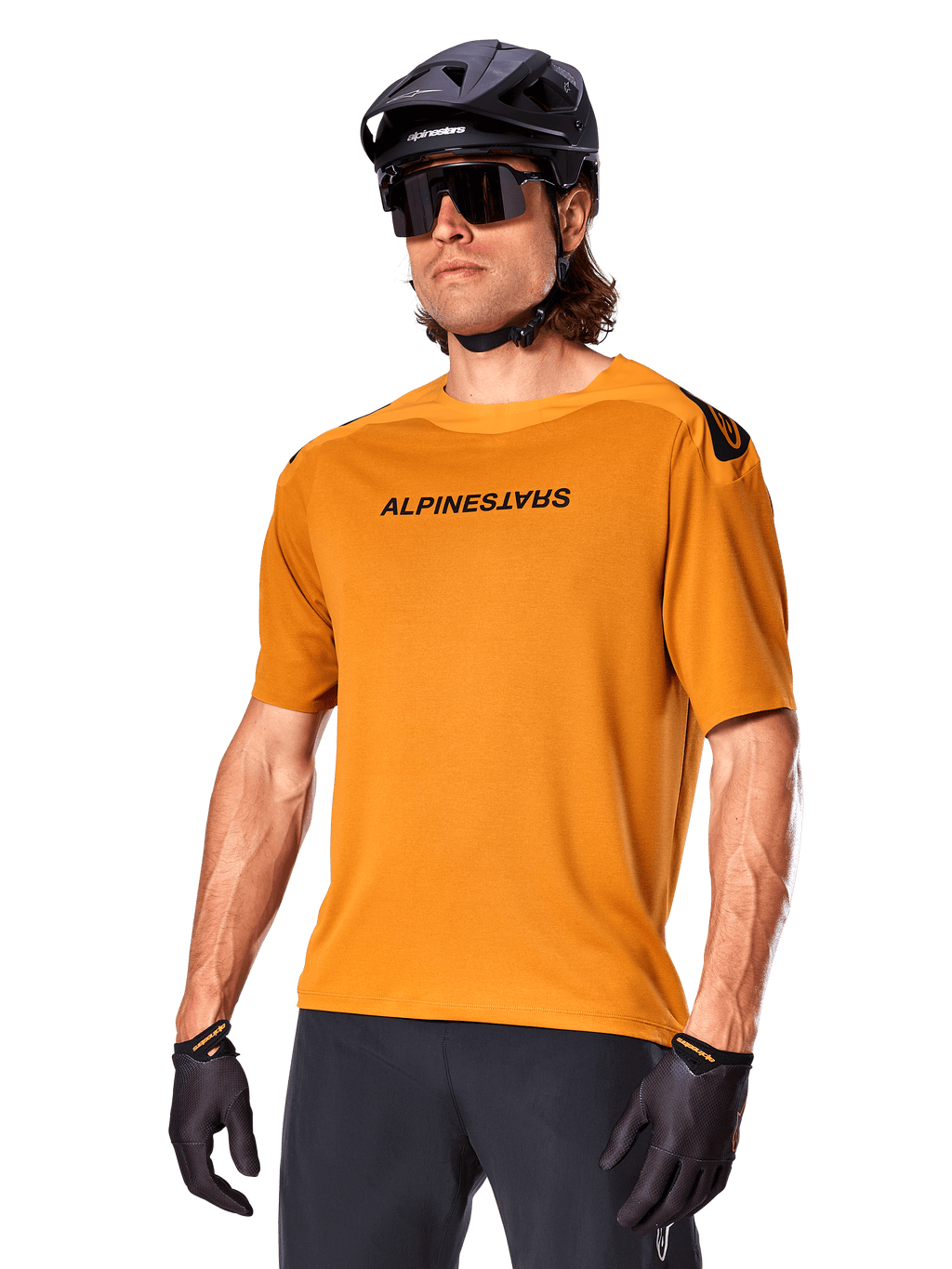Jersey Alpinestars A-Aria Polartec Switch, jersey de MTB de manga corta, color oro oscuro con logotipos en negro, usado por un modelo con casco negro, gafas de sol y guantes de ciclismo, ropa de ciclismo de montaña de alto rendimiento