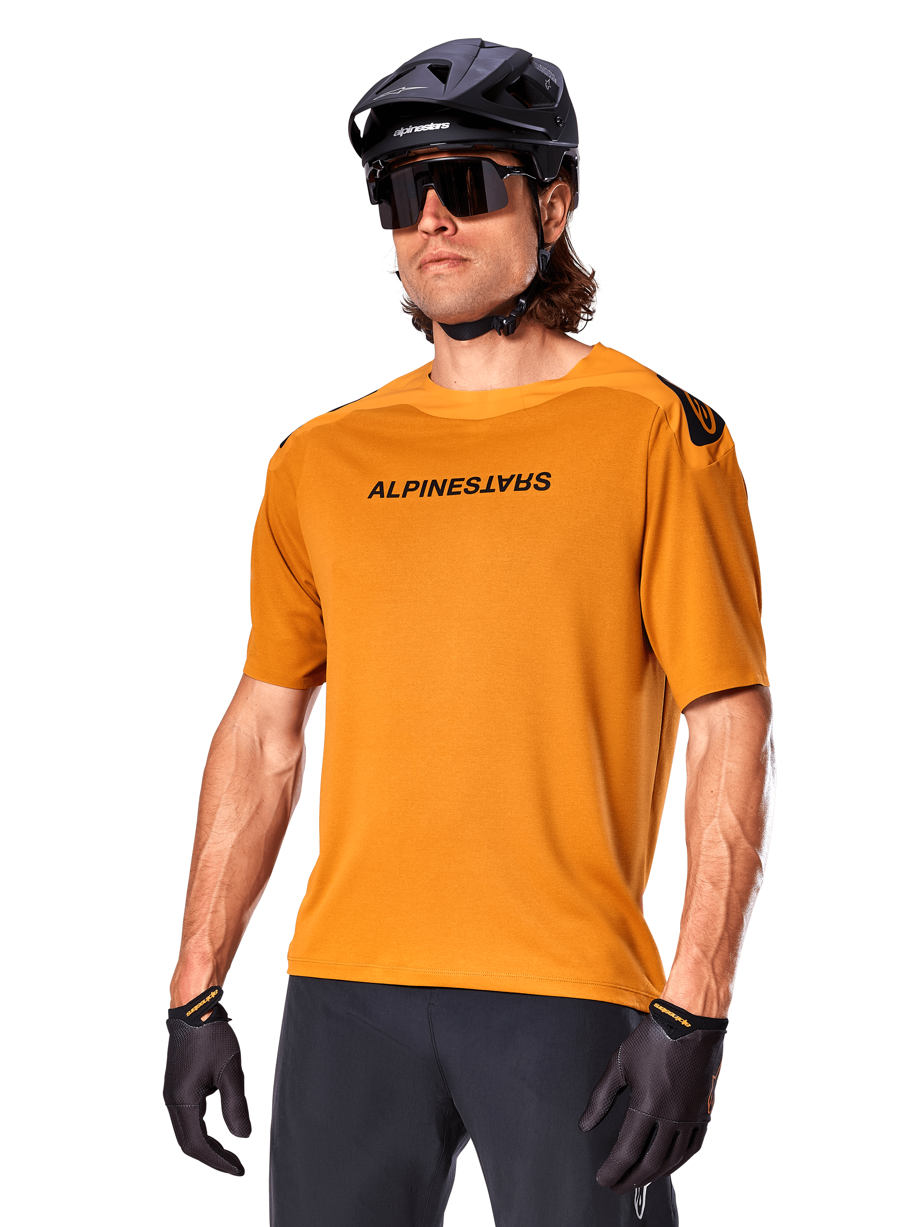 Jersey Alpinestars A-Aria Polartec Switch, jersey de MTB de manga corta, color oro oscuro con logotipos en negro, usado por un modelo con casco negro, gafas de sol y guantes de ciclismo, ropa de ciclismo de montaña de alto rendimiento