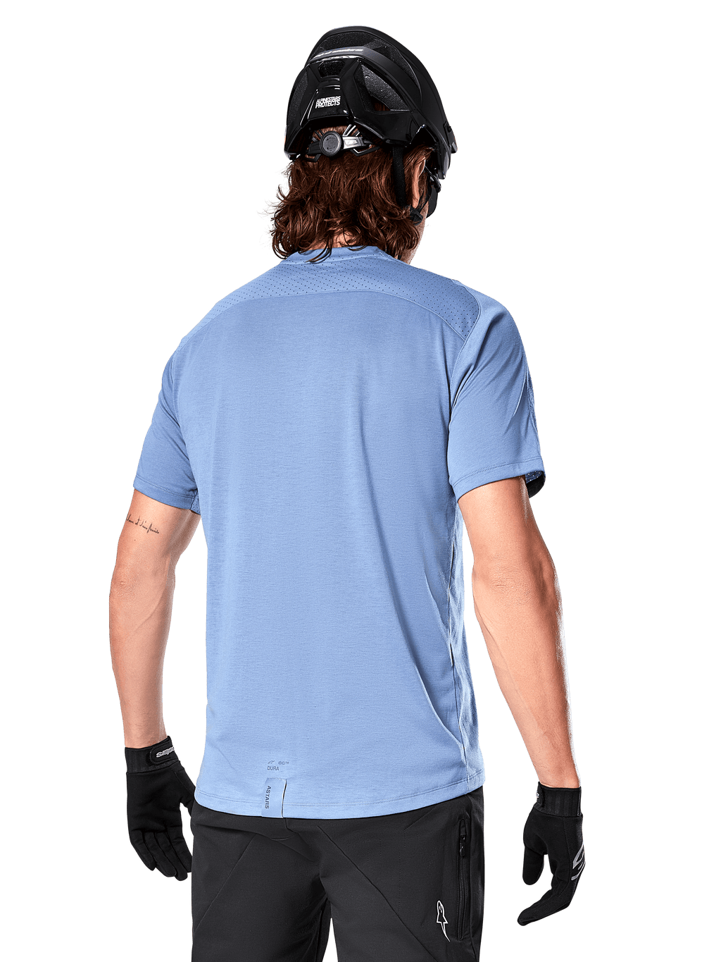 Alpinestars A-Dura Dri Astar Short Sleeve Jersey, jersey de MTB, color Azul Infinity, vista trasera que muestra paneles de ventilación de malla en los hombros y una parte trasera más larga, usado con casco de MTB y guantes negros, equipamiento de ciclismo de alto rendimiento