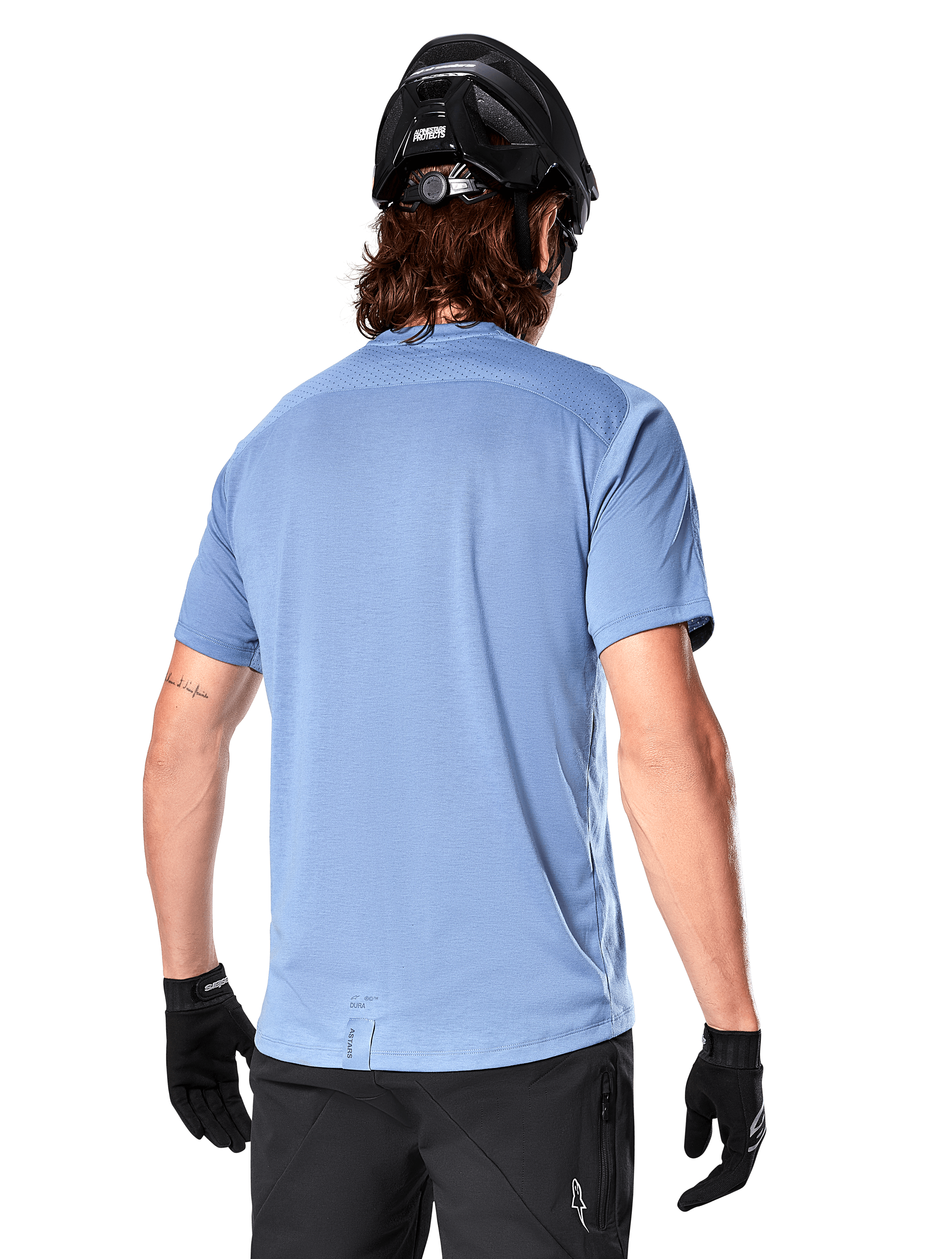 Alpinestars A-Dura Dri Astar Short Sleeve Jersey, jersey de MTB, color Azul Infinity, vista trasera que muestra paneles de ventilación de malla en los hombros y una parte trasera más larga, usado con casco de MTB y guantes negros, equipamiento de ciclismo de alto rendimiento