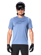 Ciclista de montaña con el jersey de manga corta Alpinestars A-Dura Dri Astar en azul Infinity, con un logotipo sutil en el pecho y paneles de malla, complementado con casco negro, gafas de sol y guantes negros para un conjunto técnico de ciclismo