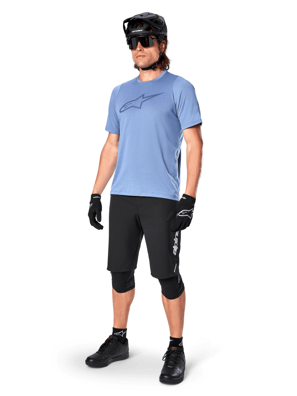Ciclista masculino con el jersey de manga corta Alpinestars A-Dura Dri Astar en Infinity Blue, combinado con pantalones cortos de MTB negros, casco negro, gafas de sol, rodilleras y guantes, equipamiento completo de ciclismo de montaña