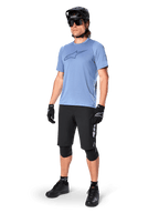 Ciclista masculino con el jersey de manga corta Alpinestars A-Dura Dri Astar en Infinity Blue, combinado con pantalones cortos de MTB negros, casco negro, gafas de sol, rodilleras y guantes, equipamiento completo de ciclismo de montaña