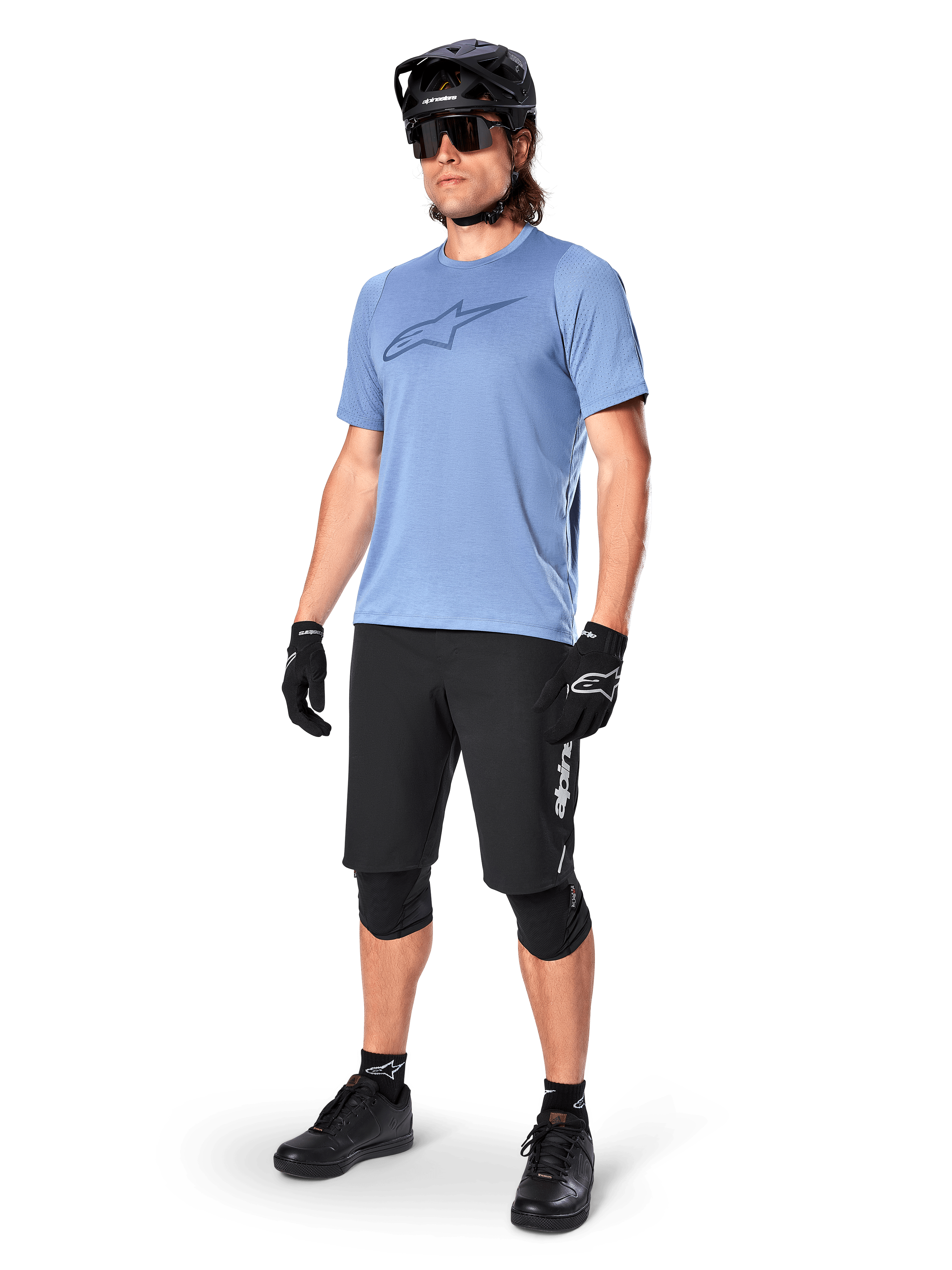Ciclista masculino con el jersey de manga corta Alpinestars A-Dura Dri Astar en Infinity Blue, combinado con pantalones cortos de MTB negros, casco negro, gafas de sol, rodilleras y guantes, equipamiento completo de ciclismo de montaña