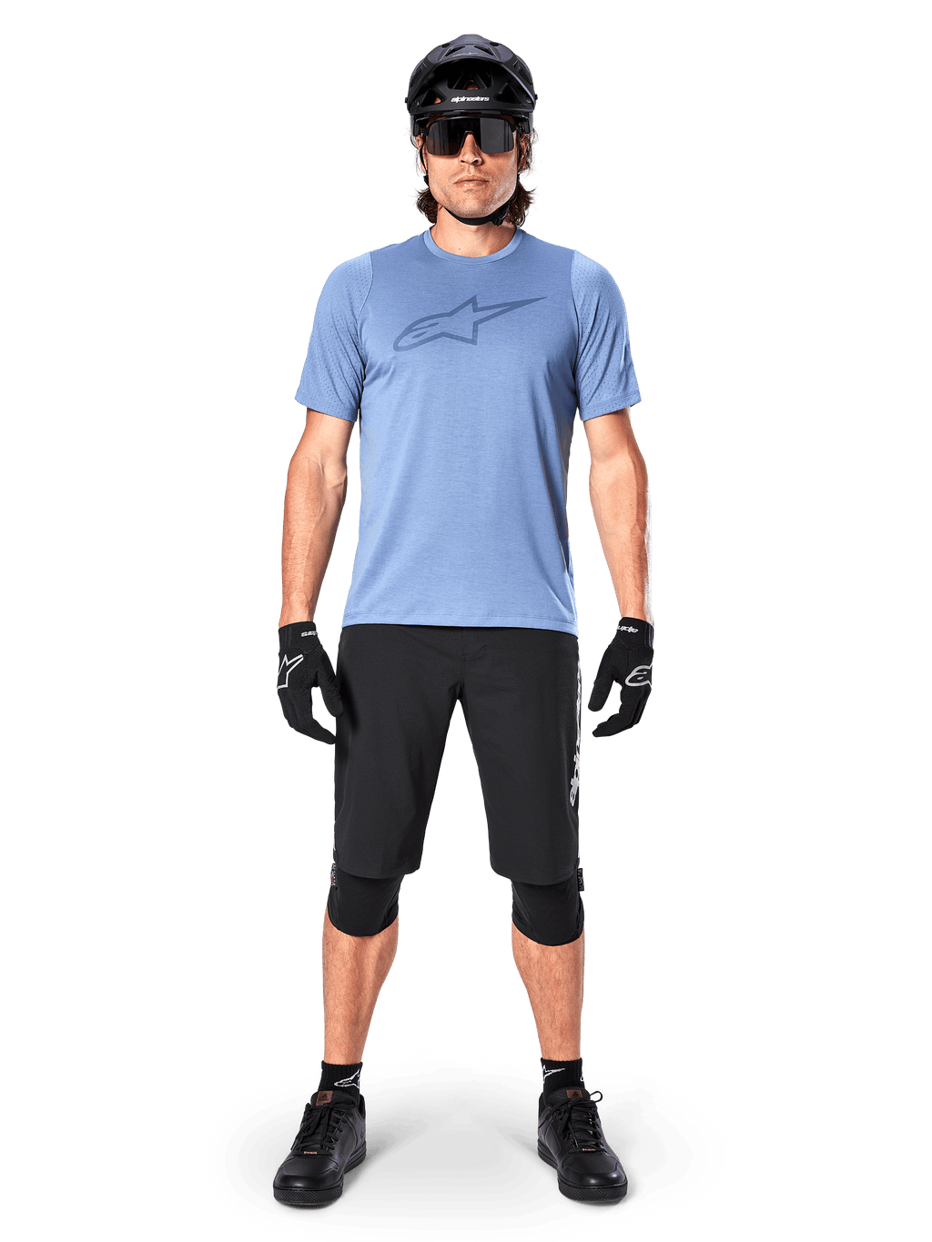 Ciclista de montaña masculino con el Jersey Alpinestars A-Dura Dri Astar de manga corta en color Infinity Blue, con un destacado logotipo de Astars en el pecho, combinado con pantalones cortos de MTB negros, casco negro, gafas de sol y equipo de protección para ciclismo todoterreno