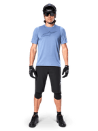 Ciclista de montaña masculino con el Jersey Alpinestars A-Dura Dri Astar de manga corta en color Infinity Blue, con un destacado logotipo de Astars en el pecho, combinado con pantalones cortos de MTB negros, casco negro, gafas de sol y equipo de protección para ciclismo todoterreno