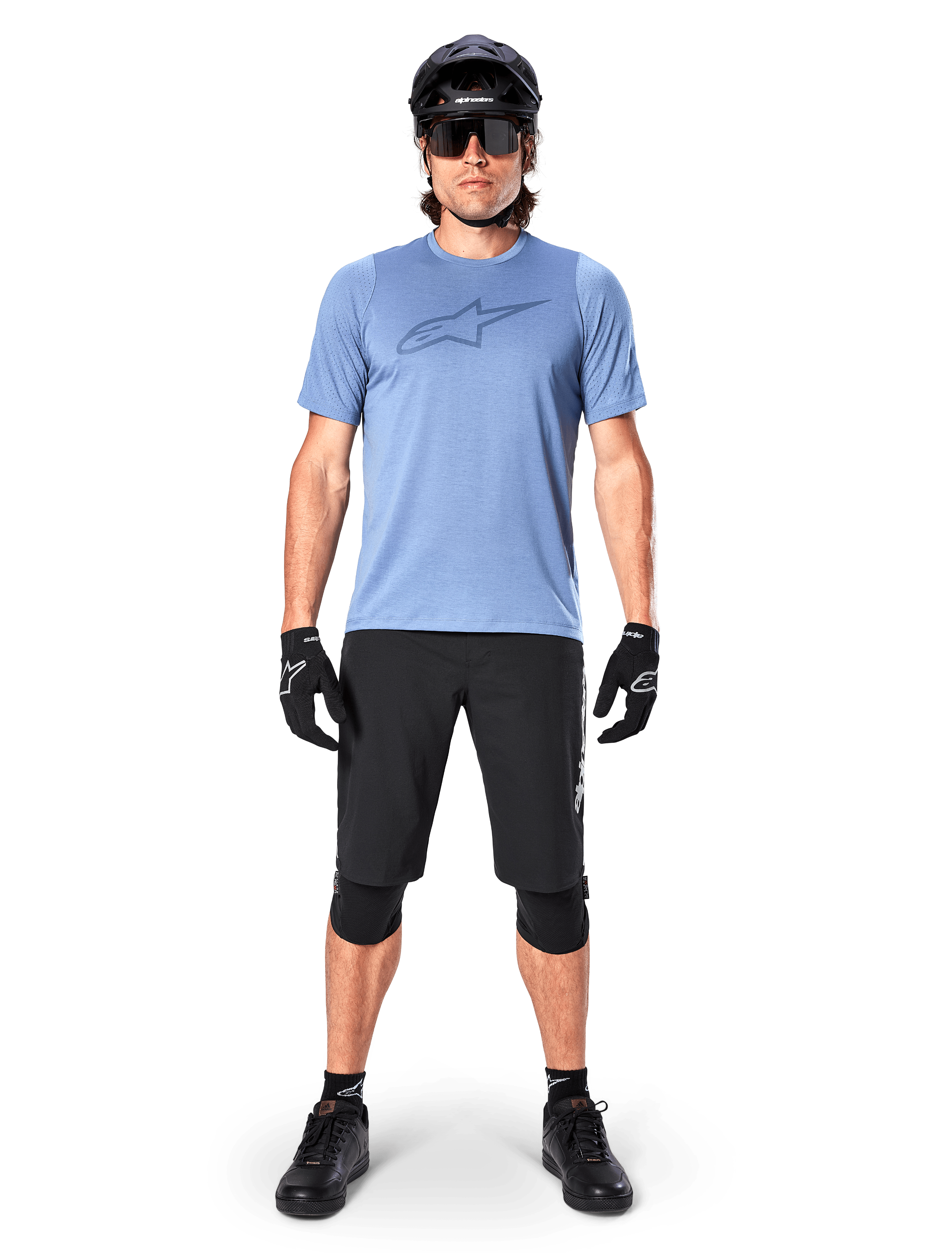 Ciclista de montaña masculino con el Jersey Alpinestars A-Dura Dri Astar de manga corta en color Infinity Blue, con un destacado logotipo de Astars en el pecho, combinado con pantalones cortos de MTB negros, casco negro, gafas de sol y equipo de protección para ciclismo todoterreno