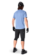 Jersey de manga corta Alpinestars A-Dura Dri Astar, Infinity Blue, vista posterior, combinado con pantalones cortos de bicicleta de montaña y casco negros, ropa técnica de ciclismo con tejido que absorbe la humedad y parte trasera más larga