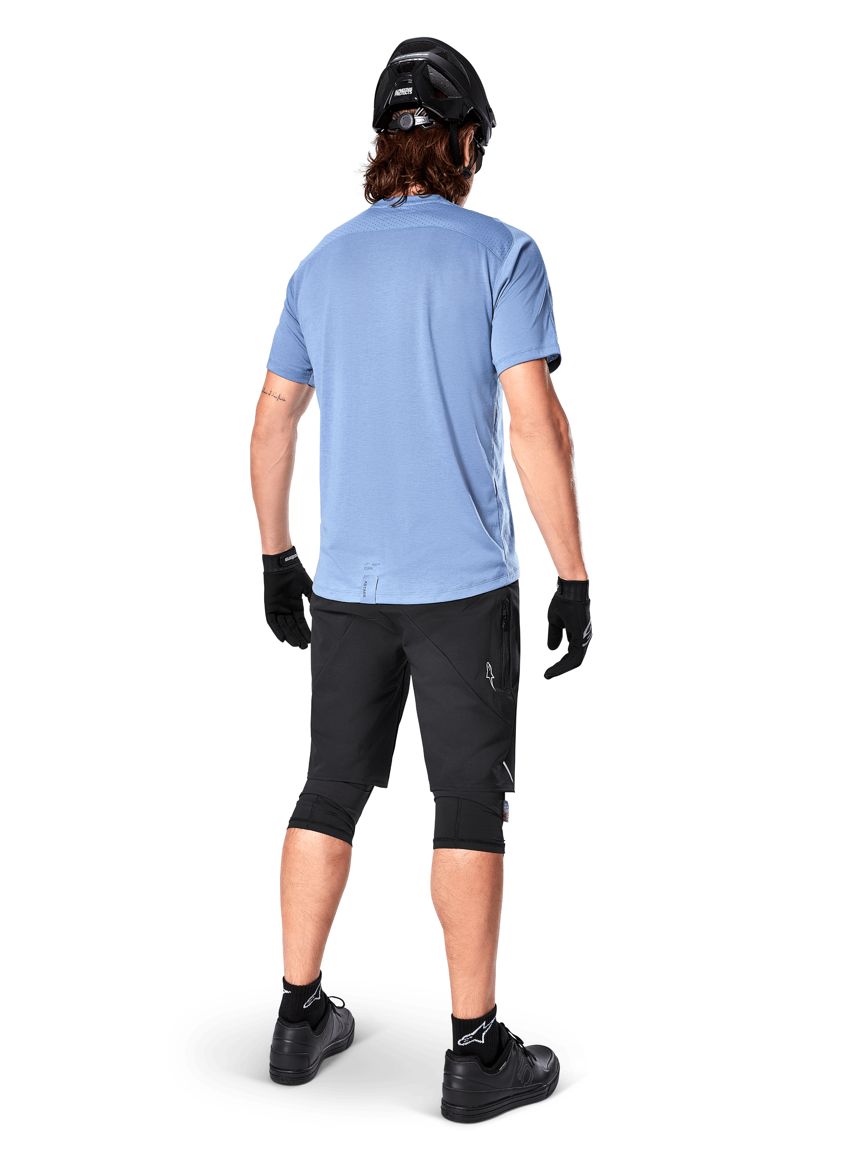 Jersey de manga corta Alpinestars A-Dura Dri Astar, Infinity Blue, vista posterior, combinado con pantalones cortos de bicicleta de montaña y casco negros, ropa técnica de ciclismo con tejido que absorbe la humedad y parte trasera más larga
