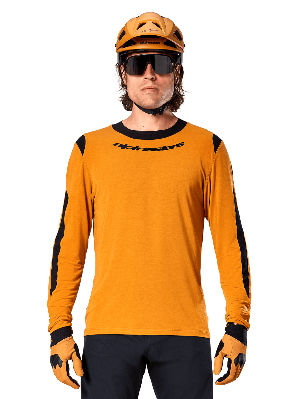 Modelo masculino con jersey Alpinestars A-Dura Dri Wool de manga larga en color Dark Gold, coordinado con casco de MTB y guantes dorados a juego, paneles de malla negros en hombros y mangas, logotipo Alpinestars en el pecho, gafas de sol y pantalones oscuros, equipamiento técnico para bicicleta de montaña
