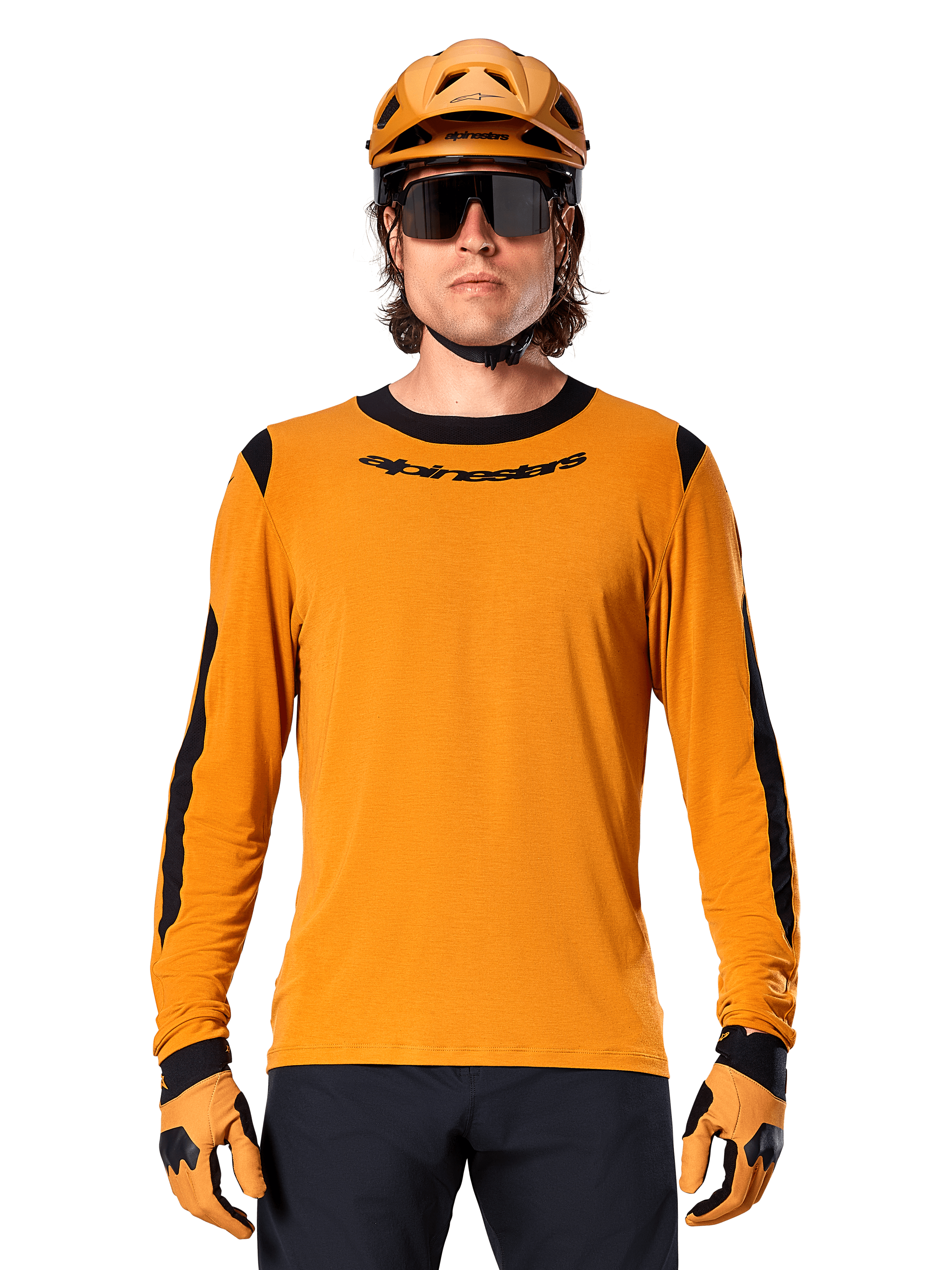 Modelo masculino con jersey Alpinestars A-Dura Dri Wool de manga larga en color Dark Gold, coordinado con casco de MTB y guantes dorados a juego, paneles de malla negros en hombros y mangas, logotipo Alpinestars en el pecho, gafas de sol y pantalones oscuros, equipamiento técnico para bicicleta de montaña