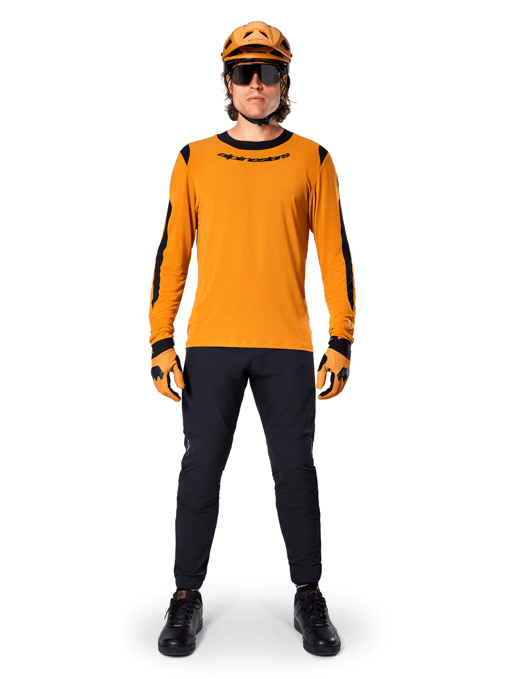 Ciclista de montaña con el jersey de manga larga Alpinestars A-Dura Dri Wool, color oro oscuro con detalles negros en el cuello y las mangas, combinado con pantalones negros, casco y guantes dorados a juego y gafas de sol negras, equipamiento profesional para ciclismo de montaña