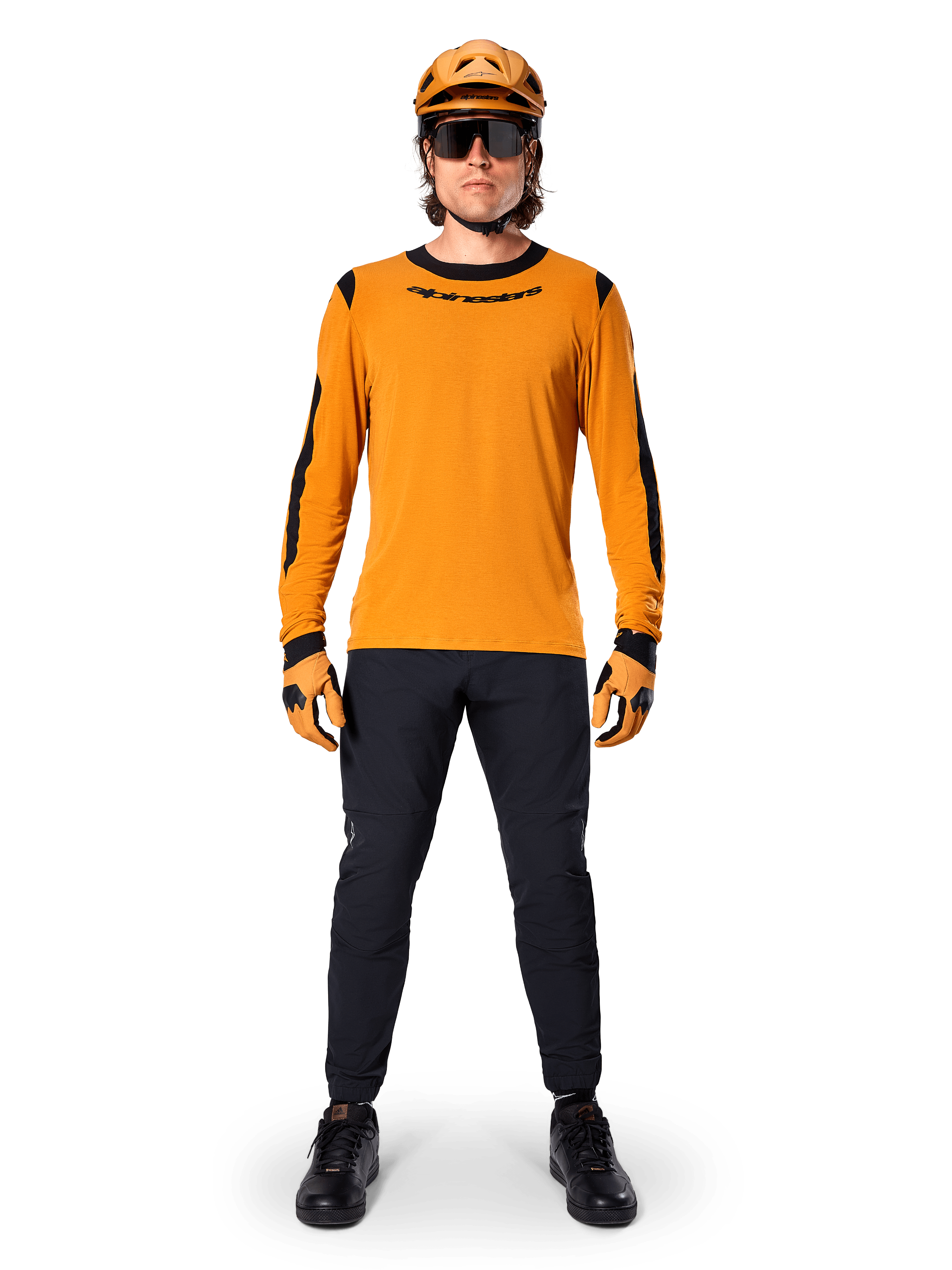 Ciclista de montaña con el jersey de manga larga Alpinestars A-Dura Dri Wool, color oro oscuro con detalles negros en el cuello y las mangas, combinado con pantalones negros, casco y guantes dorados a juego y gafas de sol negras, equipamiento profesional para ciclismo de montaña