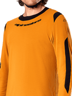 Jersey de manga larga Alpinestars A-Dura Dri Wool, color oro oscuro, primer plano que muestra el cuello redondo negro con logo y paneles de ventilación de malla negra en los hombros y brazos, ropa de alto rendimiento para bicicleta de montaña