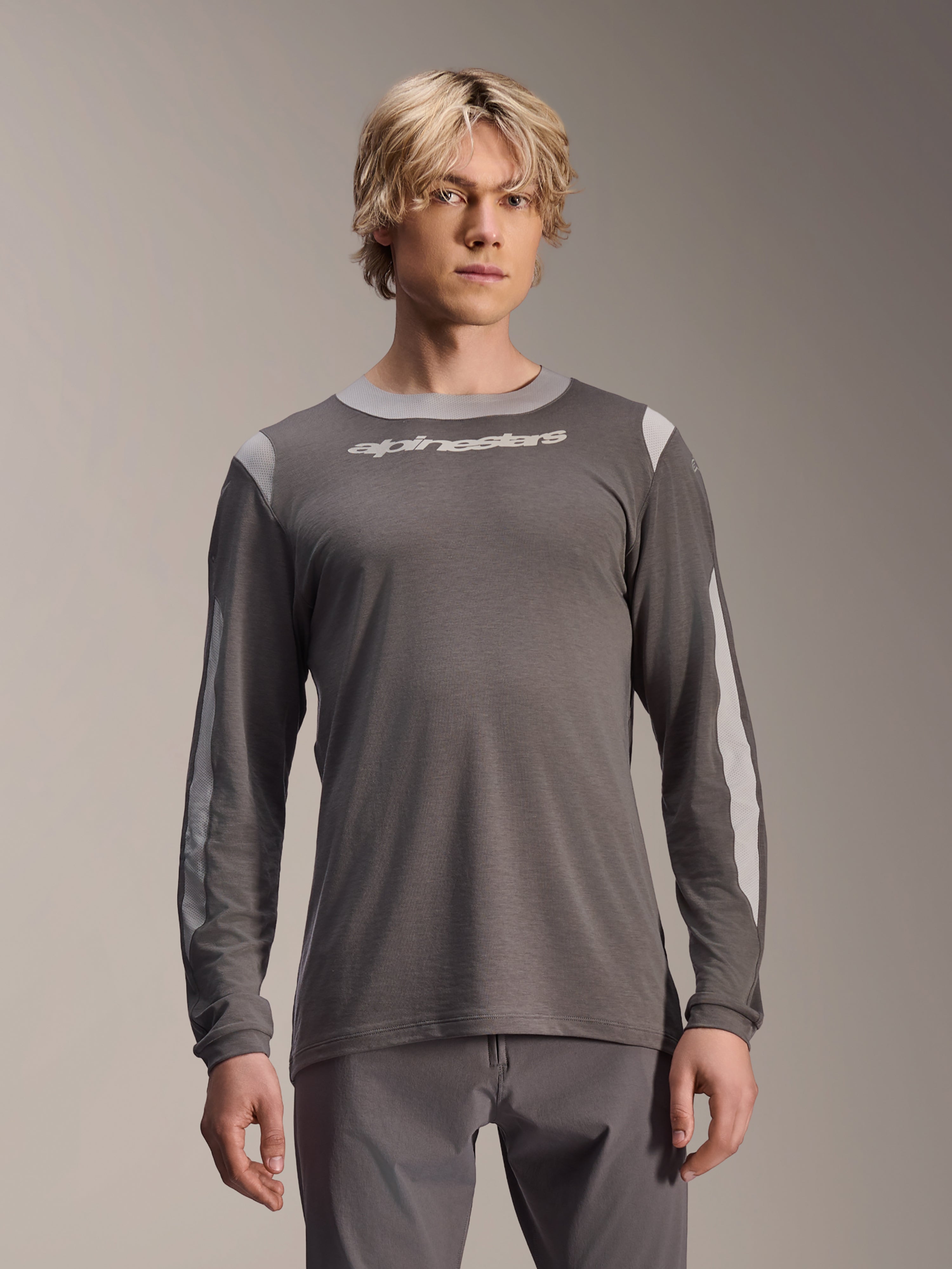 Alpinestars A-Dura Dri Wool Jersey de manga larga, gris oscuro, usado por un modelo masculino, con paneles de malla gris claro en los hombros y las mangas, logotipo blanco en el pecho, equipamiento de alto rendimiento para bicicleta de montaña