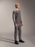 Modelo masculino vistiendo el jersey de manga larga Alpinestars A-Dura Dri Wool en gris oscuro, combinado con pantalones grises a juego y calzado negro, con paneles de malla gris claro en los hombros y las mangas, equipamiento técnico de MTB para ciclismo de montaña