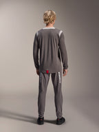 Alpinestars A-Dura Dri Wool Jersey de manga larga, gris oscuro, vista trasera en modelo, con paneles de malla gris claro en los hombros y el cuello, dobladillo trasero más largo con una pequeña etiqueta roja de la marca, combinado con pantalones de ciclismo grises a juego.