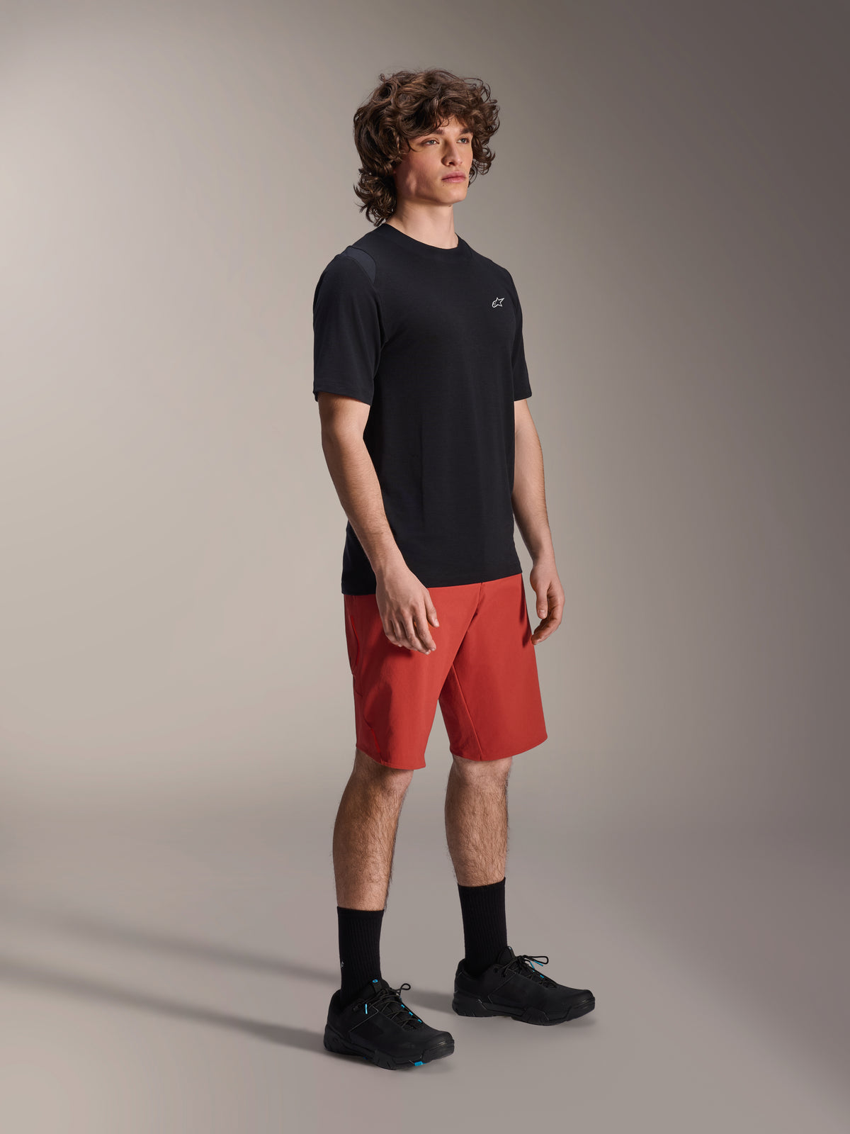Modelo masculino vistiendo shorts Alpinestars A-Dura Elite en naranja oscuro y jersey de manga corta A-Dura Dri Wool en negro, equipamiento de alto rendimiento para bicicleta de montaña, combinado con calcetines y zapatillas negras, diseño deportivo para ciclismo de montaña