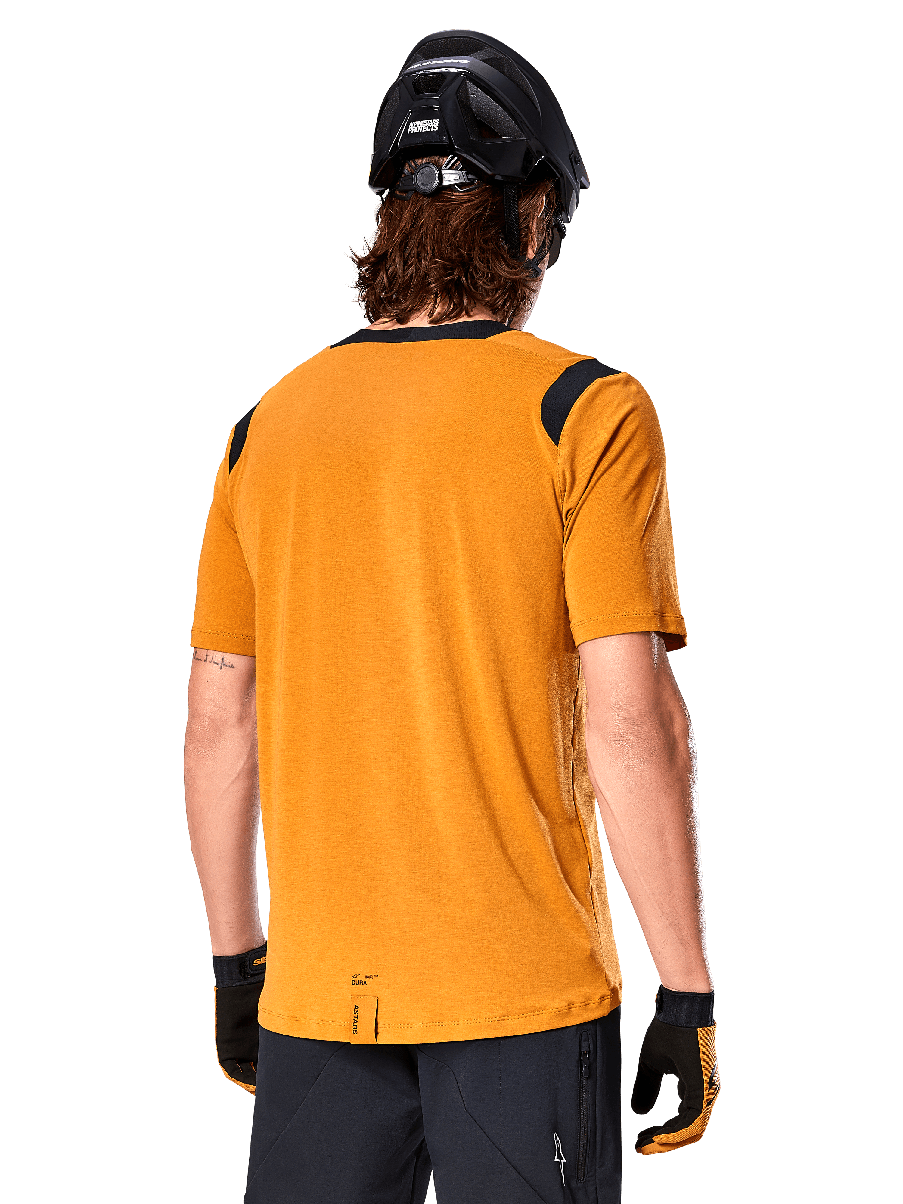 Alpinestars A-Dura Dri Wool Jersey de manga corta, oro oscuro, vista trasera de un hombre usando el jersey de manga corta con paneles de malla negra en los hombros, combinado con un casco de MTB negro y guantes, equipamiento de ciclismo de montaña de ajuste regular.