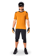 Jersey de manga corta Alpinestars A-Dura Dri Wool en color Dark Gold, jersey de mountain bike usado con pantalones cortos negros y equipo de protección, tejido amarillo mostaza con cuello y detalles en los hombros en negro, ropa de ciclismo de alto rendimiento para rodar por senderos.