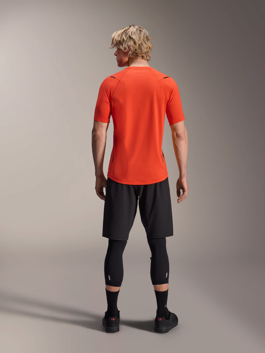 Alpinestars A-Aria Astar Jersey, jersey de MTB de manga corta, Spicy Orange, vista posterior que muestra el ajuste de rendimiento y la cola caída más larga, combinado con pantalones cortos de ciclismo y mallas negras