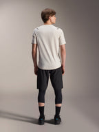 Modelo masculino visto desde atrás con el jersey de manga corta Alpinestars A-Aria Astar en color Ecru, combinado con pantalones cortos de MTB negros y mallas protectoras, con diseño de cola caída y ajuste de rendimiento para ciclismo por senderos todoterreno.