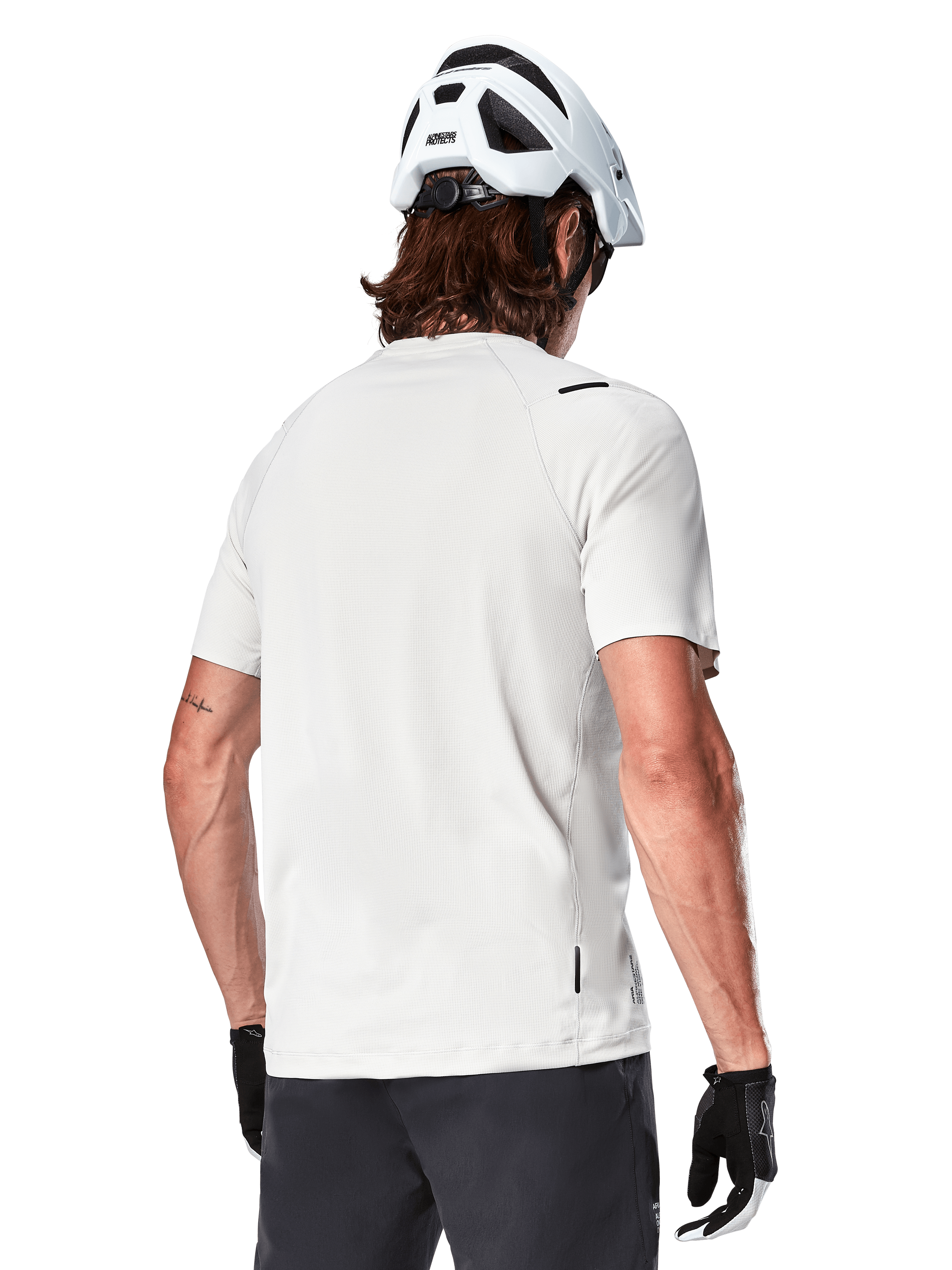 Alpinestars A-Aria Astar Jersey, manga corta, blanco (White Dove), vista trasera de este jersey de ciclismo de montaña ligero y transpirable, usado con casco blanco y guantes de ciclismo negros, con una parte trasera más larga para mayor cobertura