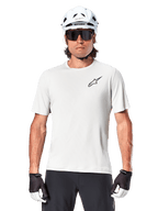 Ciclista con jersey de manga corta Alpinestars A-Aria Astar, color White Dove con pequeño logotipo Astar negro en el pecho, casco de ciclismo blanco, gafas de sol negras y guantes blancos y negros, equipamiento de alto rendimiento para MTB y conducción fuera de carretera
