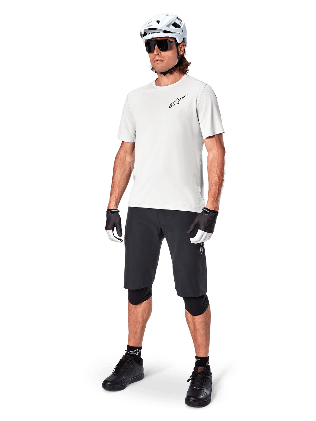 Ciclista de MTB con el jersey Alpinestars A-Aria Astar de manga corta en color White Dove, combinado con pantalones cortos de montaña negros, casco blanco y rodilleras negras, con un pequeño logotipo negro en el pecho, equipamiento de ciclismo coordinado para el rendimiento en senderos