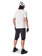 Ciclista con el jersey de manga corta Alpinestars A-Aria Astar en color White Dove, vista trasera, combinado con pantalones cortos de MTB negros, rodilleras y casco blanco, equipamiento ligero y transpirable para ciclismo de montaña todoterreno