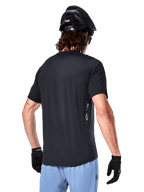 Alpinestars A-Dura Oscar Jersey, jersey de ciclismo de manga corta, negro, vista trasera del ciclista, combinado con pantalones cortos azul claro y casco de MTB negro, pequeño logo blanco en el lateral, ropa técnica para ciclismo de montaña