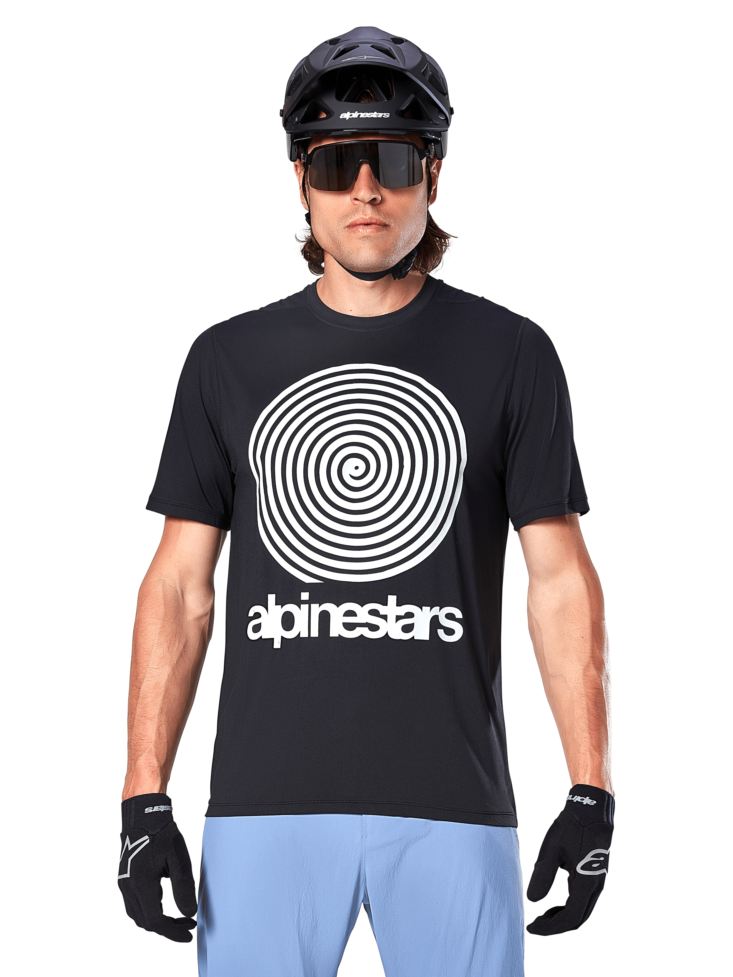 Alpinestars Jersey A-Dura Oscar, jersey de MTB de manga corta, negro, con un gran gráfico de espiral vintage de Oscar en blanco en el pecho, usado con casco de ciclismo negro, gafas de sol, guantes negros y pantalones cortos azul claro, equipamiento de ciclismo de montaña de inspiración clásica