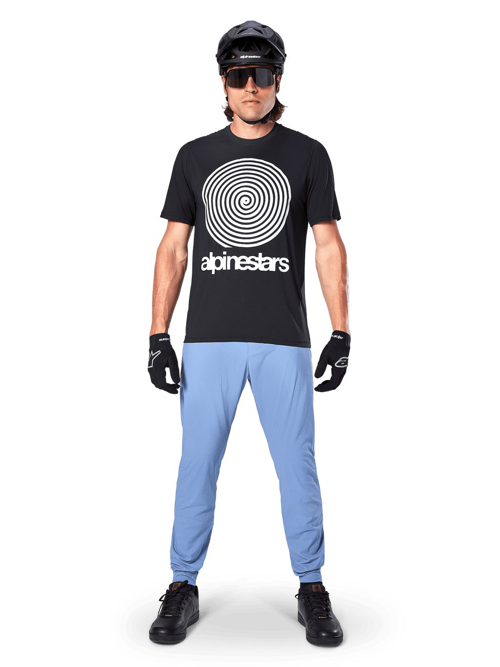 Alpinestars A-Dura Oscar Jersey - Manga Corta, jersey de MTB negro con un gran gráfico blanco de la espiral vintage de Oscar y el texto de la marca, usado con pantalones azul claro, casco negro, gafas de sol y guantes negros, ropa de alto rendimiento para bicicleta de montaña