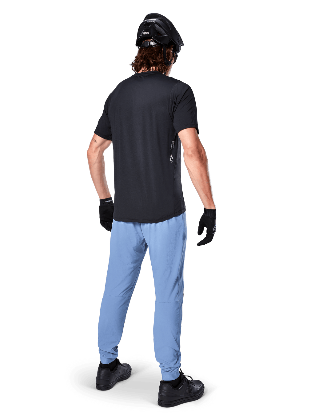Alpinestars A-Dura Oscar Jersey - Manga Corta, negro, vista trasera de un ciclista con un jersey de montaña negro, combinado con pantalones azul claro, casco negro y guantes negros, ropa técnica de MTB para rendimiento off-road