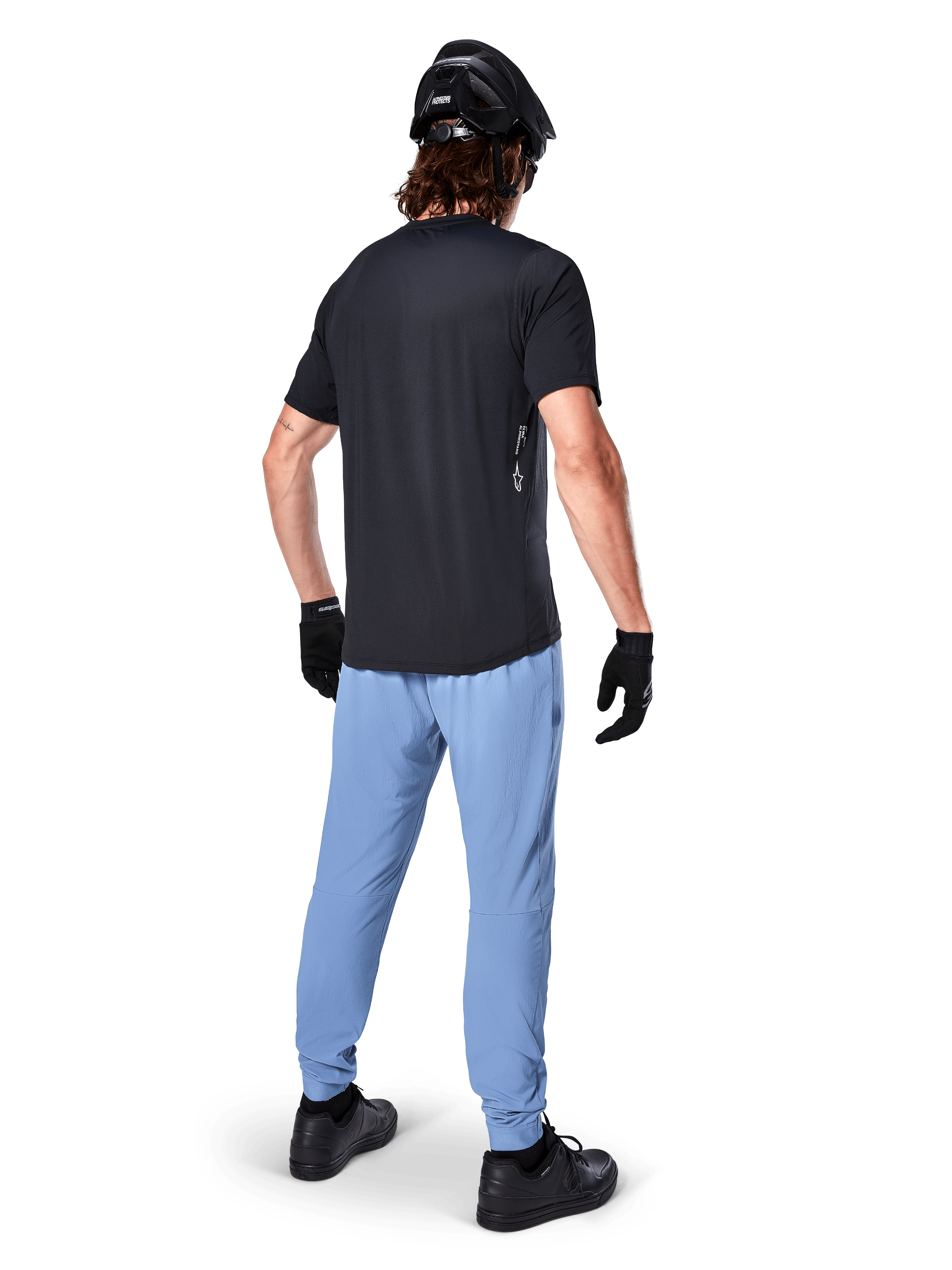 Alpinestars A-Dura Oscar Jersey - Manga Corta, negro, vista trasera de un ciclista con un jersey de montaña negro, combinado con pantalones azul claro, casco negro y guantes negros, ropa técnica de MTB para rendimiento off-road