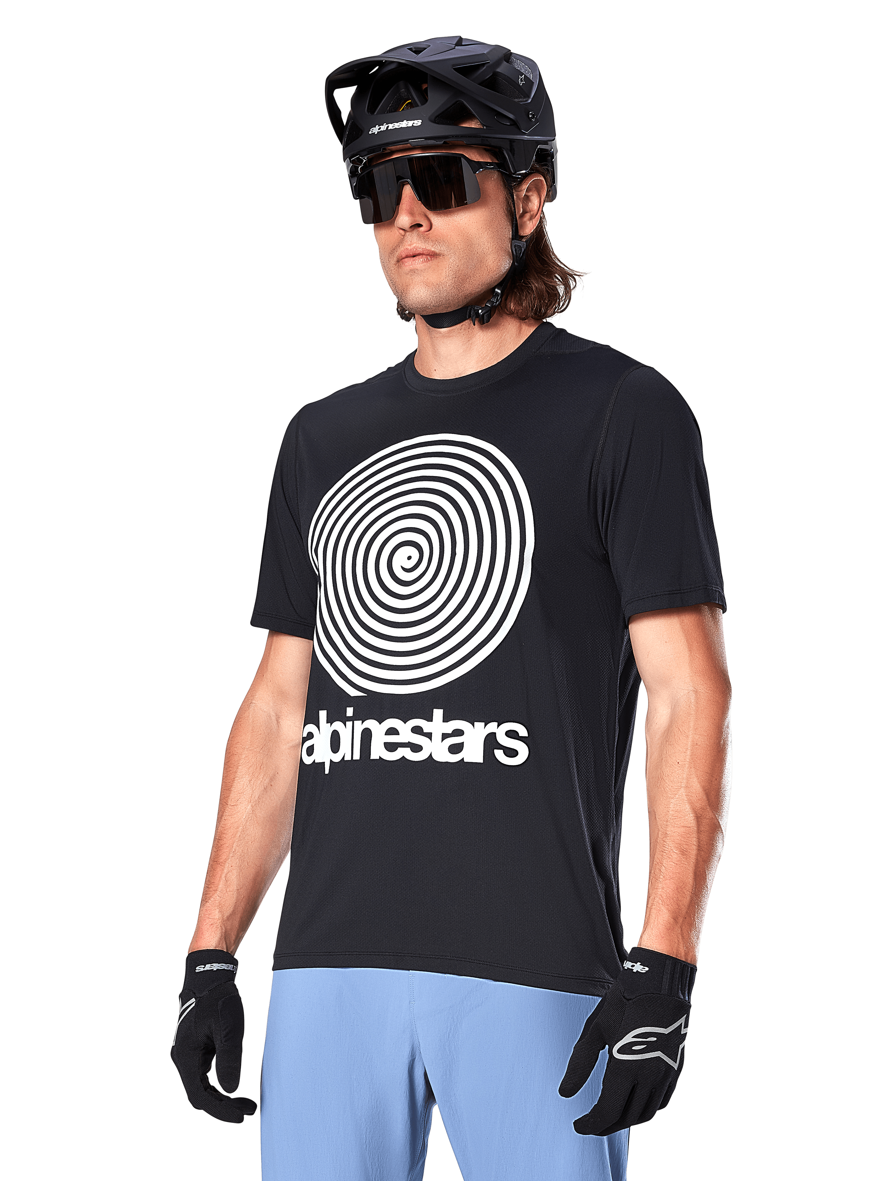 Alpinestars A-Dura Oscar Jersey - Manga Corta, negro, con un gran gráfico de espiral blanco y el logotipo de Alpinestars en el pecho, usado por un ciclista con casco de MTB negro, gafas de sol y pantalones azul claro