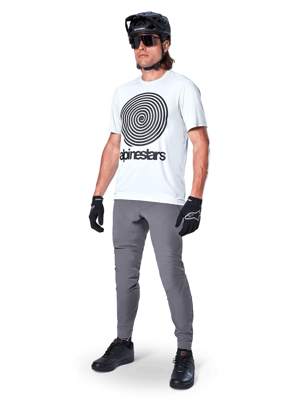 Alpinestars A-Dura Oscar Jersey - Manga Corta, White Dove con un gran gráfico de espiral negra, usado por un ciclista con pantalones de MTB grises, casco negro y guantes, ropa de ciclismo de alto rendimiento para rutas todoterreno