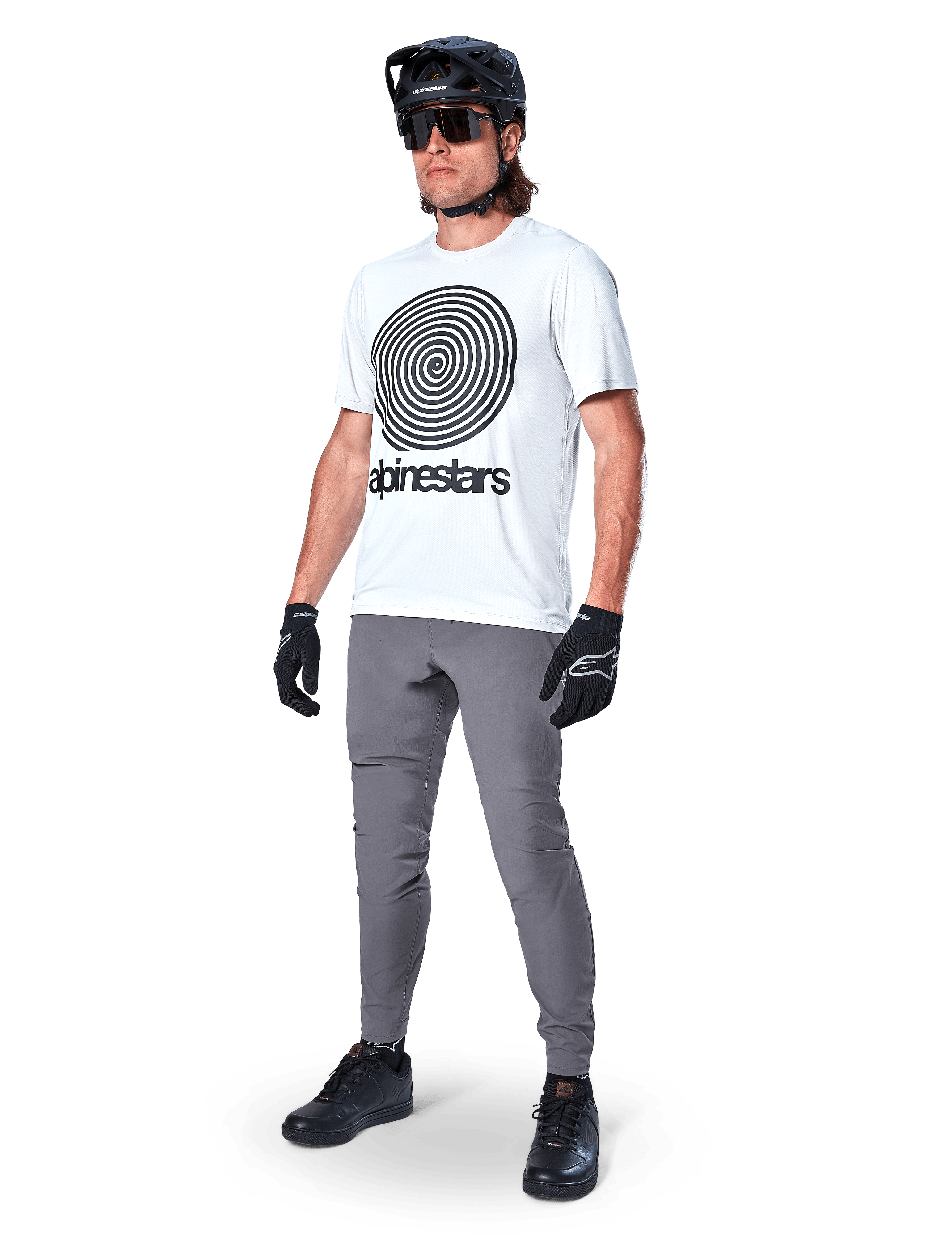 Alpinestars A-Dura Oscar Jersey - Manga Corta, White Dove con un gran gráfico de espiral negra, usado por un ciclista con pantalones de MTB grises, casco negro y guantes, ropa de ciclismo de alto rendimiento para rutas todoterreno