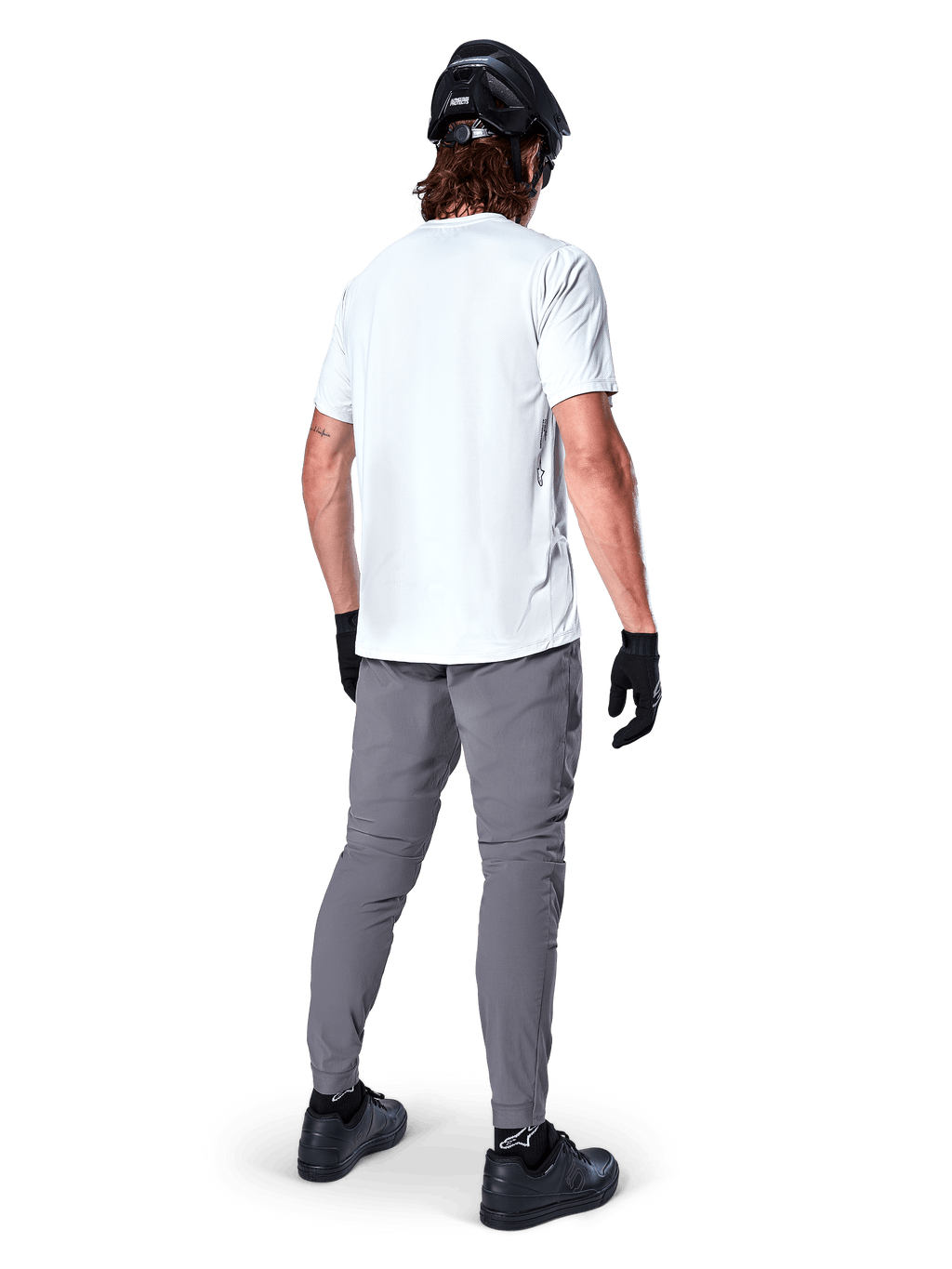 Jersey de manga corta Alpinestars A-Dura Oscar en White Dove, vista trasera de un ciclista con pantalones de ciclismo grises, casco negro y guantes, ropa técnica de bicicleta de montaña para recorridos por senderos