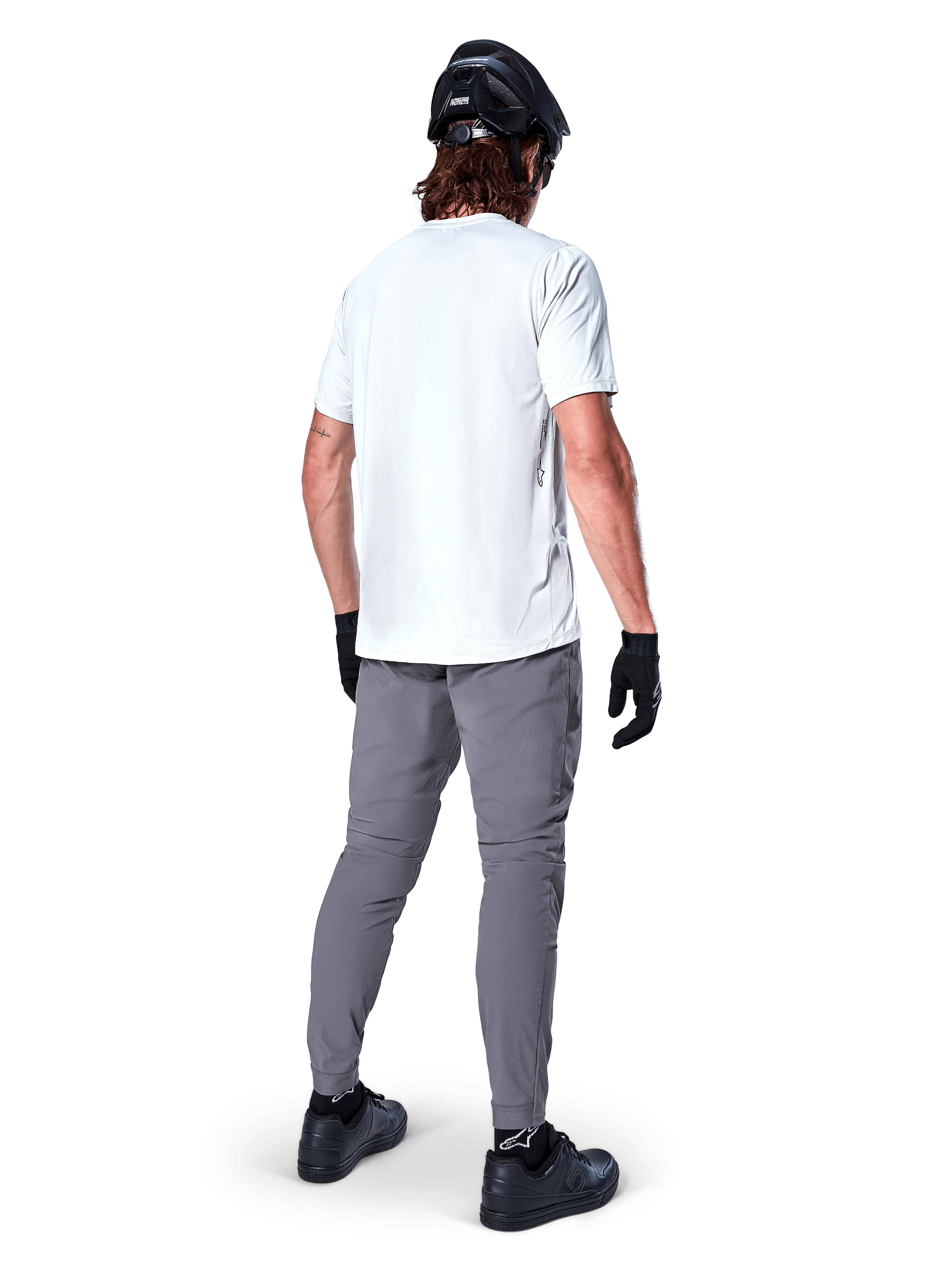 Jersey de manga corta Alpinestars A-Dura Oscar en White Dove, vista trasera de un ciclista con pantalones de ciclismo grises, casco negro y guantes, ropa técnica de bicicleta de montaña para recorridos por senderos