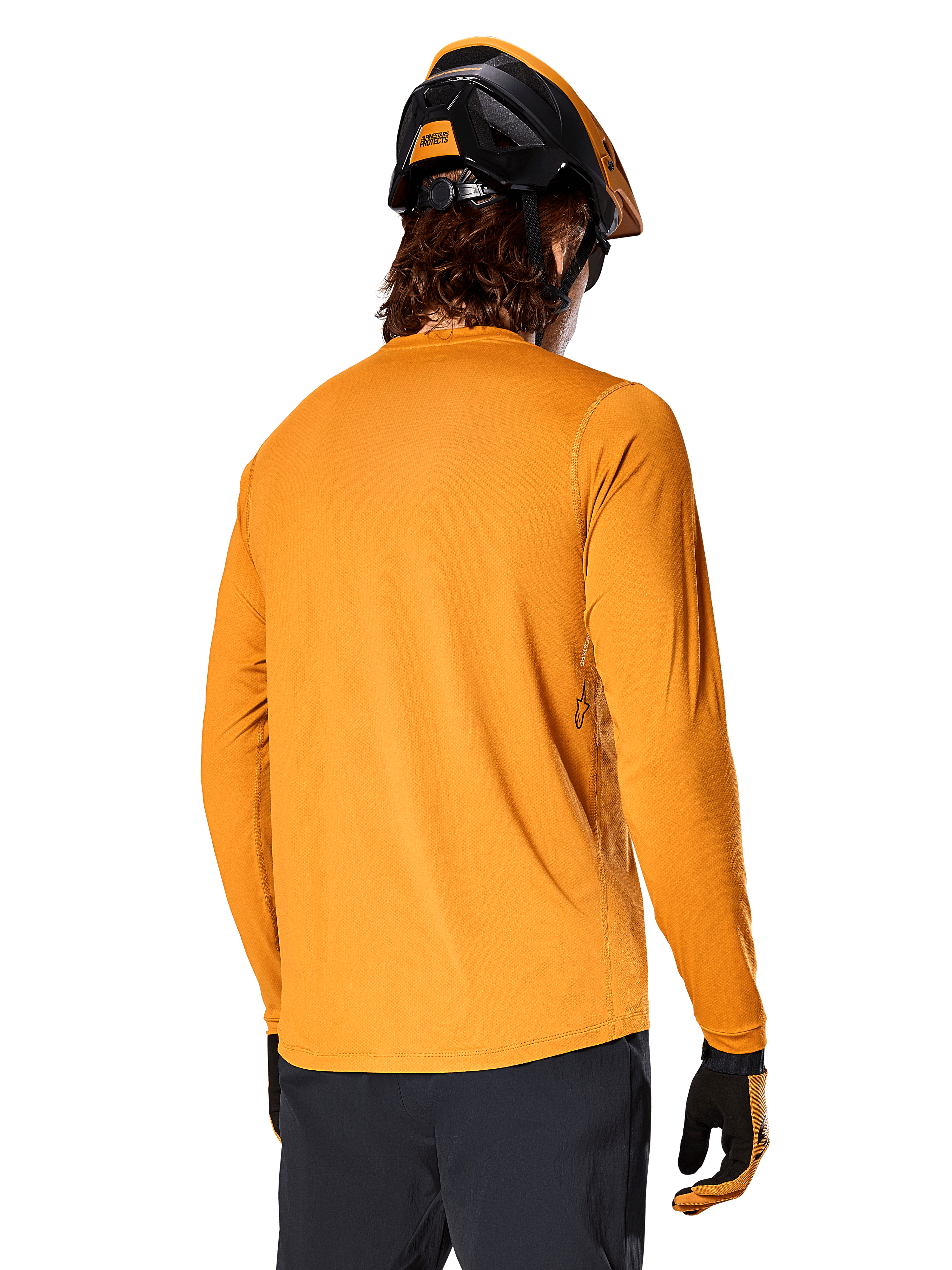 Alpinestars Jersey de manga larga A-Dura Rocker, Oro Oscuro, vista posterior del ciclista con casco de MTB negro y naranja, pantalones oscuros y guantes a juego, ropa de ciclismo de montaña de rendimiento casual