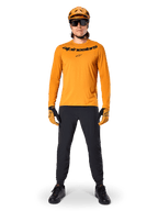 Jersey de manga larga Alpinestars A-Dura Rocker en color Dark Gold, con logotipo serigrafiado en negro en el pecho, usado con un casco de MTB dorado a juego, gafas de sol negras y pantalones negros, equipamiento profesional de ciclismo de montaña