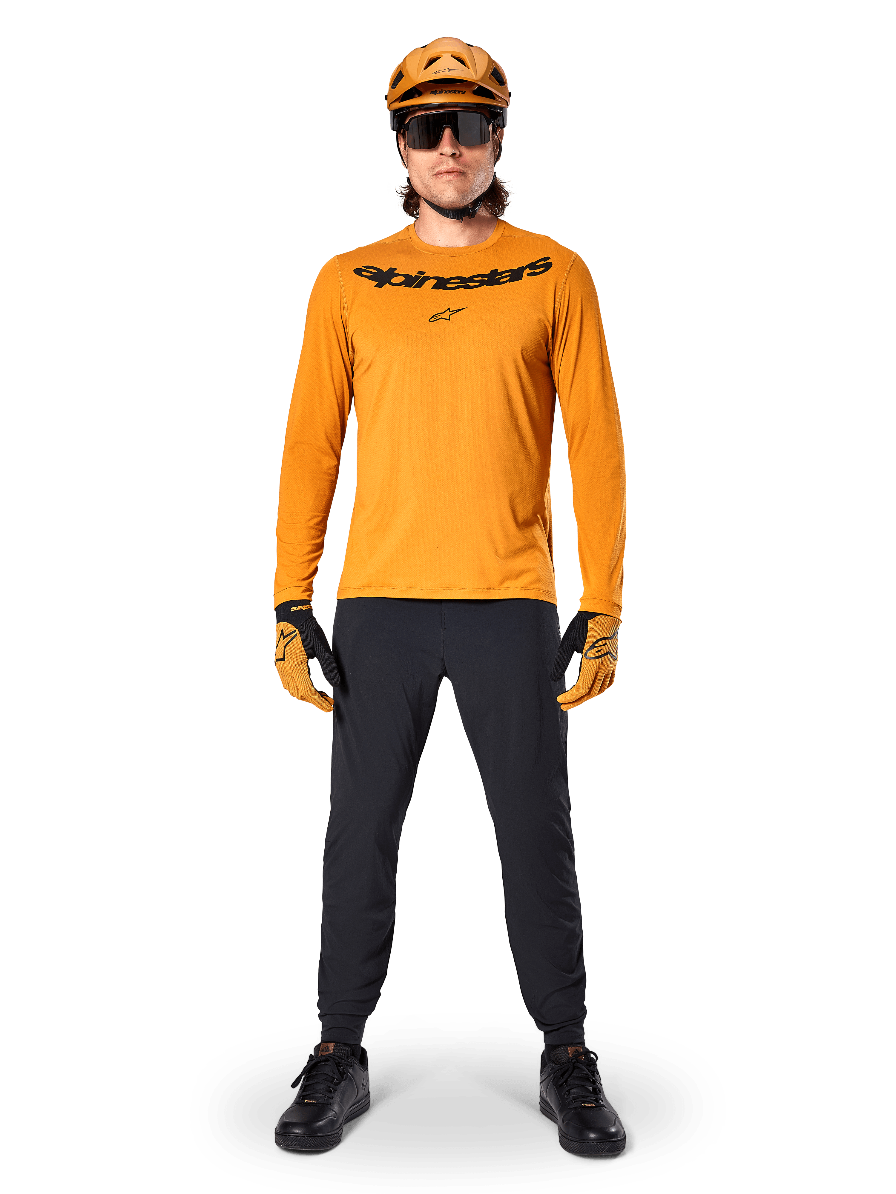 Jersey de manga larga Alpinestars A-Dura Rocker en color Dark Gold, con logotipo serigrafiado en negro en el pecho, usado con un casco de MTB dorado a juego, gafas de sol negras y pantalones negros, equipamiento profesional de ciclismo de montaña