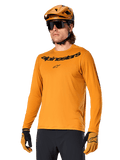 Alpinestars A-Dura Rocker Jersey de manga larga, camiseta para ciclismo de montaña MTB, color oro oscuro, persona con jersey, casco y guantes a juego, look deportivo coordinado con el logotipo de Alpinestars en el pecho