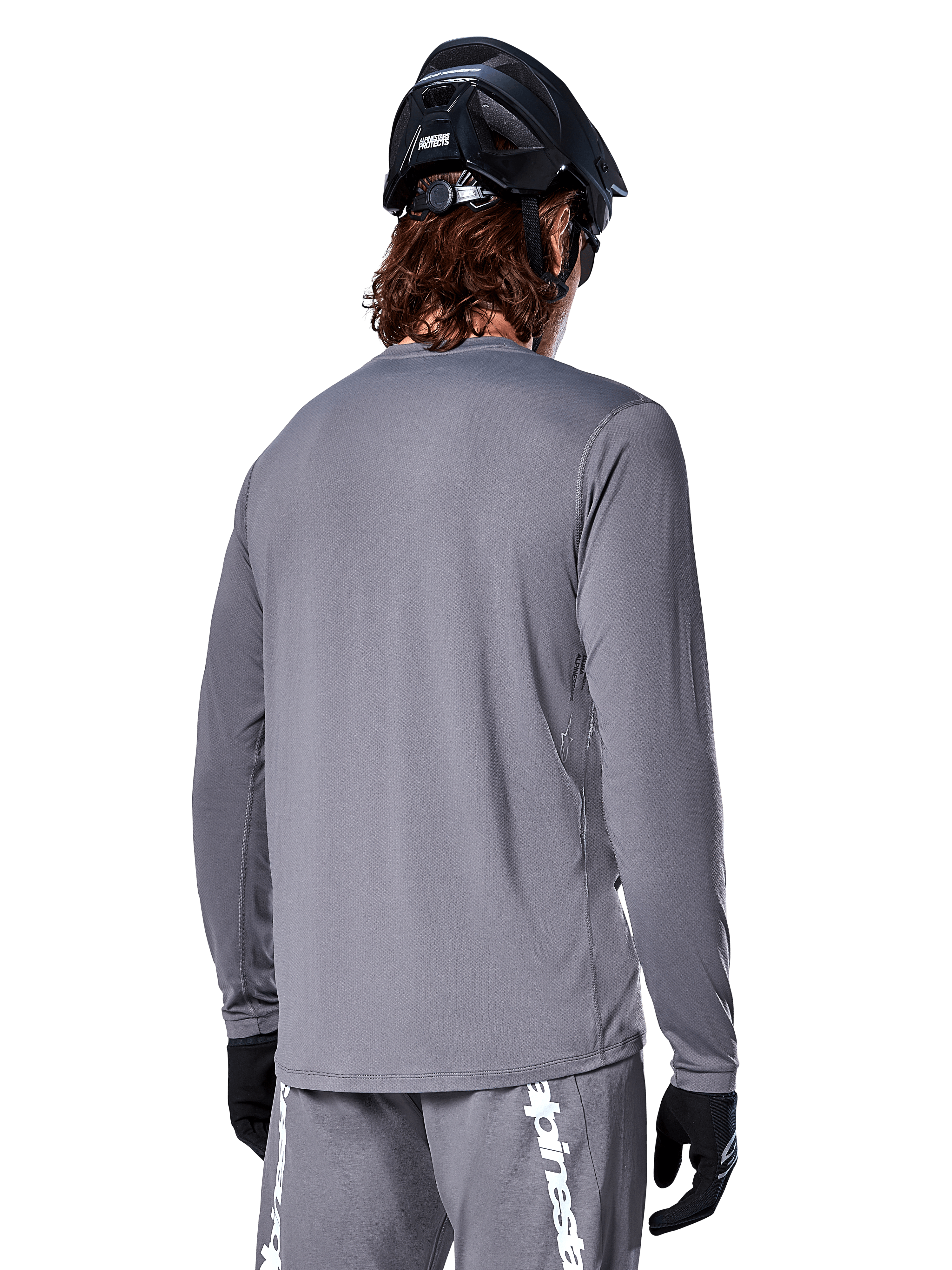 Jersey de manga larga Alpinestars A-Dura Rocker en gris oscuro, vista trasera de un ciclista de montaña, combinado con pantalones cortos grises a juego con logotipos en blanco, casco de MTB negro y guantes negros, equipamiento profesional de ciclismo todoterreno.