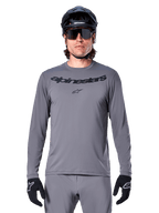 Alpinestars A-Dura Rocker Long Sleeve Jersey, jersey de MTB para hombre en gris oscuro con logotipo negro en el pecho, combinado con pantalones grises, casco negro y guantes, diseñado para ciclismo de montaña