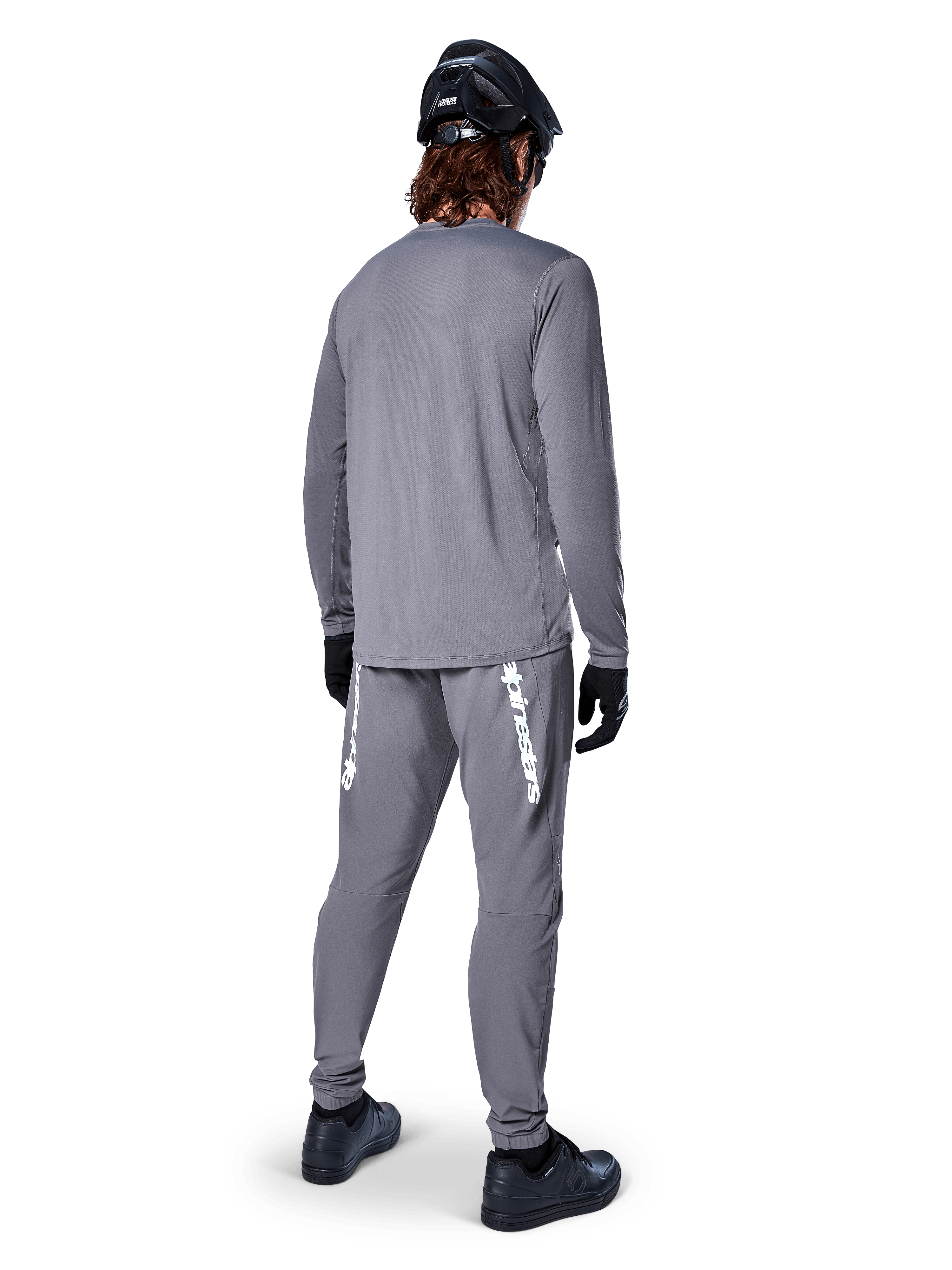 Jersey de manga larga Alpinestars A-Dura Rocker, gris oscuro, vista trasera del modelo luciendo pantalones de MTB grises a juego, casco negro y guantes negros, diseño de ropa profesional para bicicleta de montaña